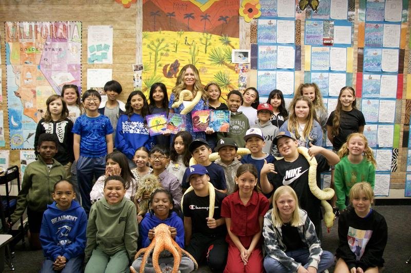 Teacher Lindsay Hill holds four children's books while standing with her students.